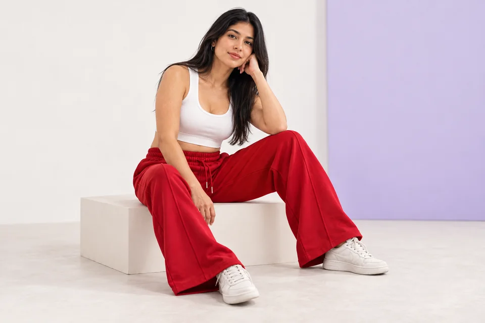 Imagen editorial generada: mujer sentada con top blanco y pantalón rojo de pierna amplia.
